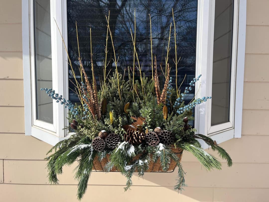 Winter window box with pine, berries, twigs, and pinecones, enhancing seasonal decor.