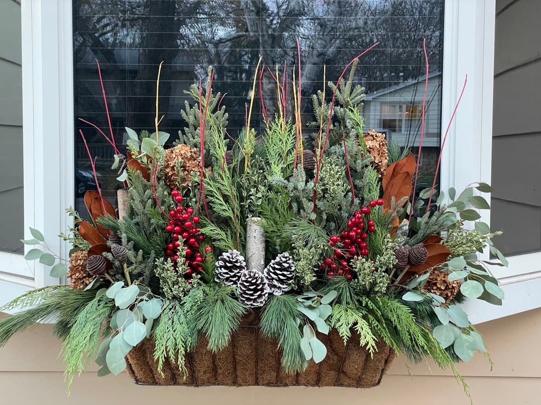Holiday window box arrangement featuring pinecones, red berries, evergreen sprigs, and decorative twigs.