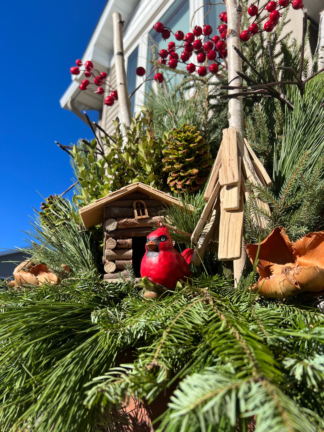 Cardinal decoration amid pine, berries, and a log cabin in a winter holiday display.