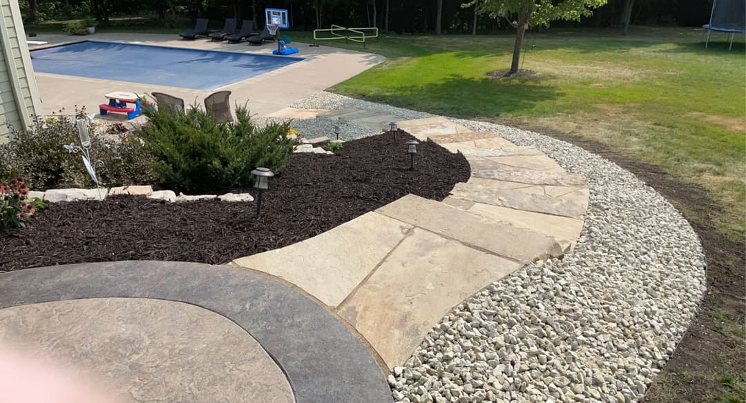 Stone pathway leading to a pool area, surrounded by mulch and decorative rocks.