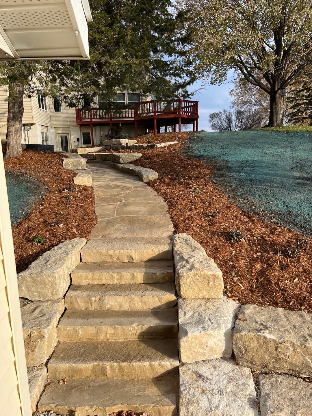Stone pathway leading to a landscaped backyard with a deck and trees.