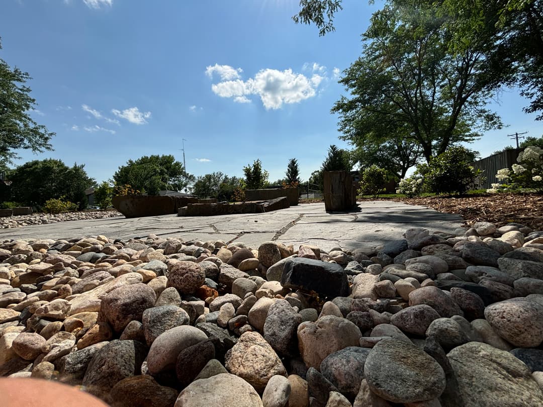 Serene outdoor space with stone pathway, greenery, and blue sky dotted with clouds.