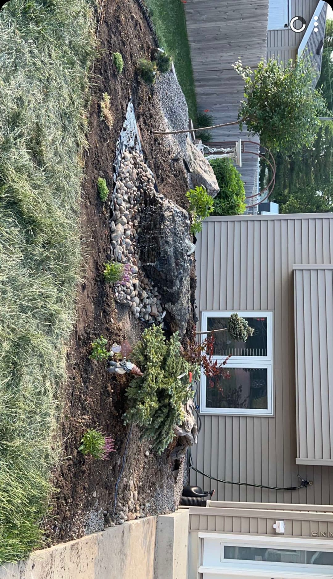 Landscaped garden featuring rocks, shrubs, and decorative stones beside a house.