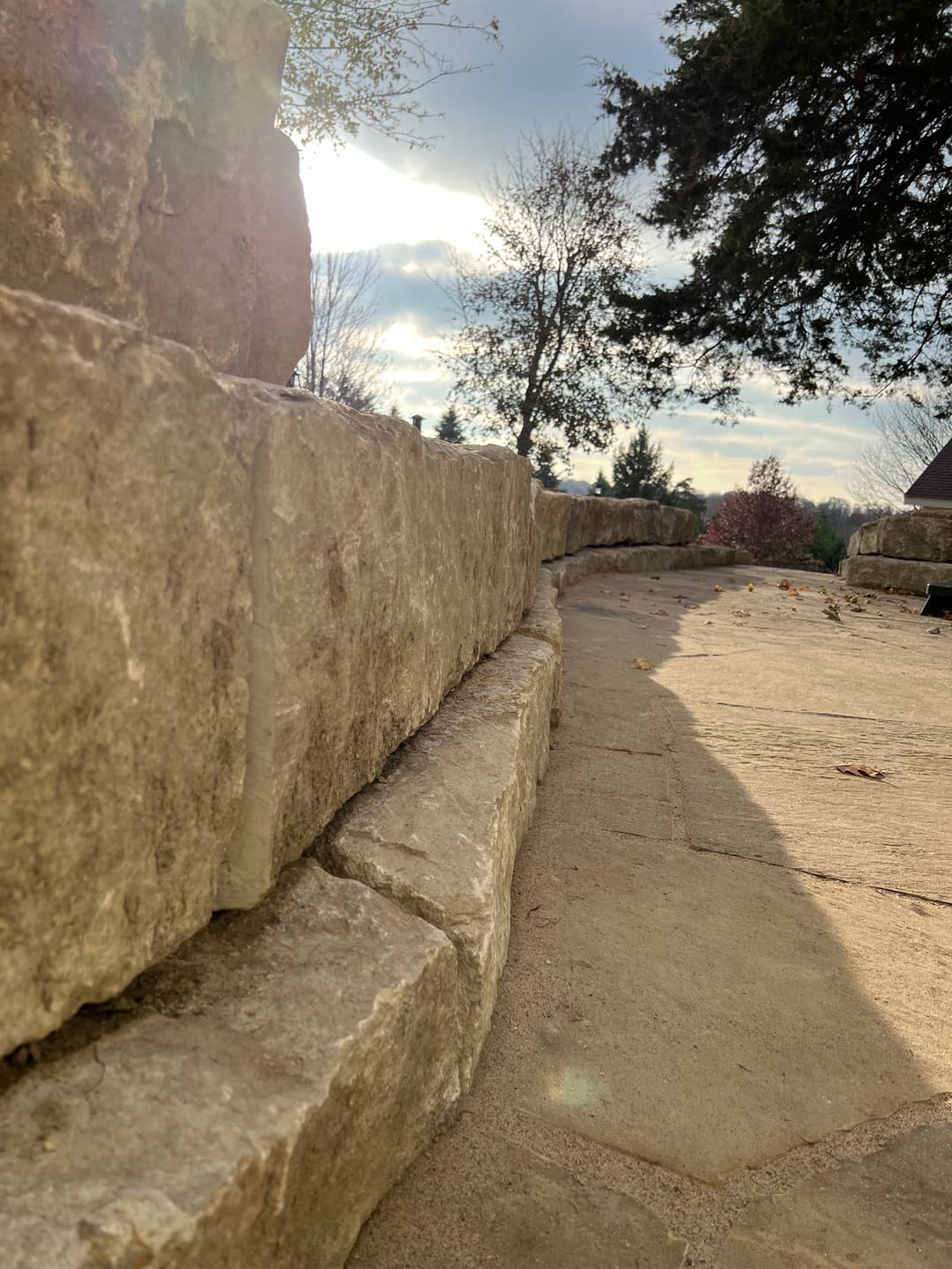 Stone wall with sunlight filtering through trees, set in a serene outdoor landscape.