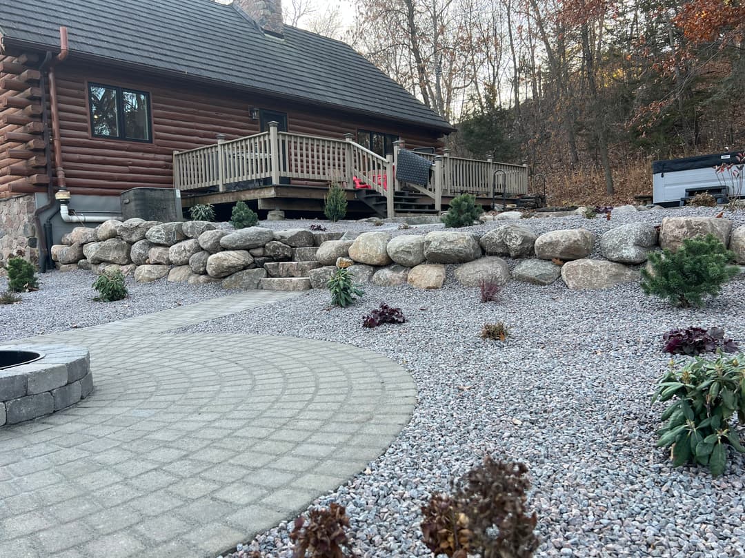 Log cabin home with stone patio, landscaped gravel yard, and garden plants in autumn.