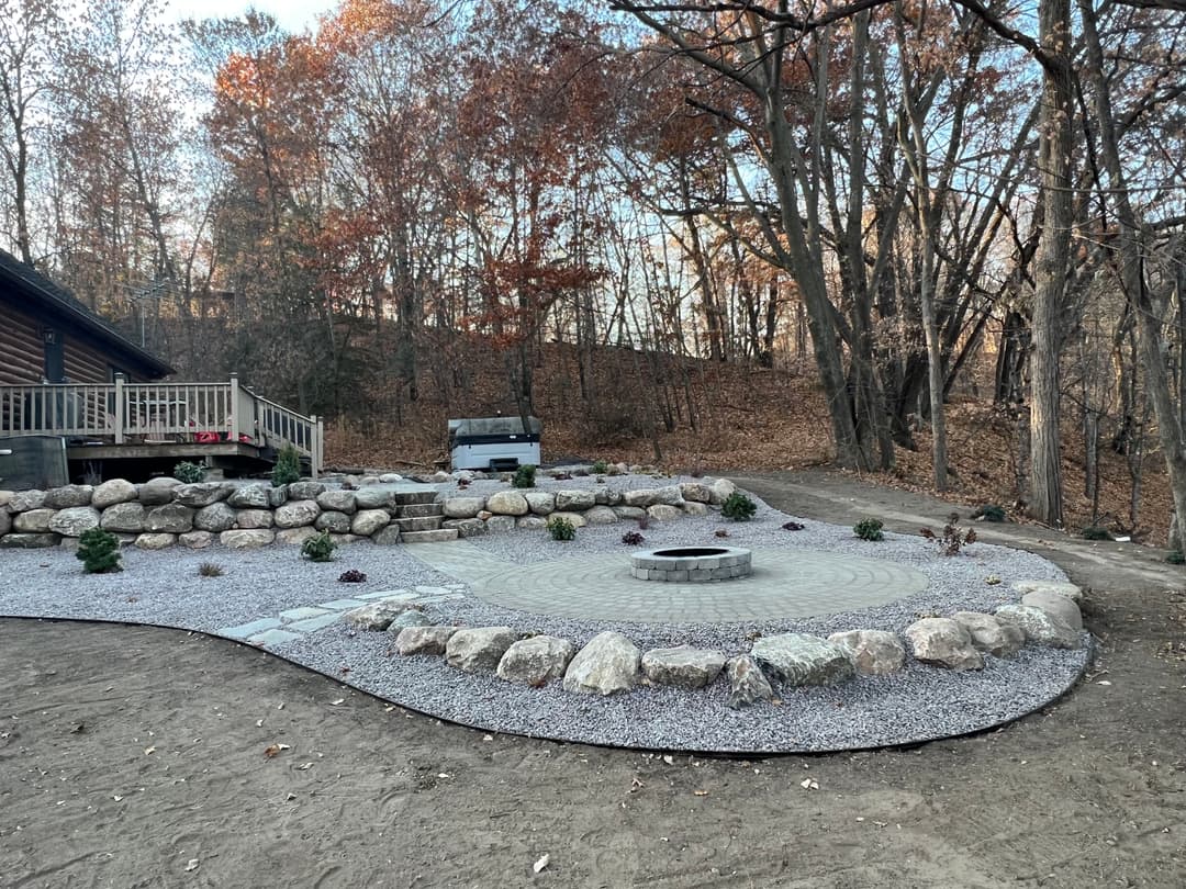 Outdoor landscaping featuring a fire pit, stone seating area, and fall foliage in the background.