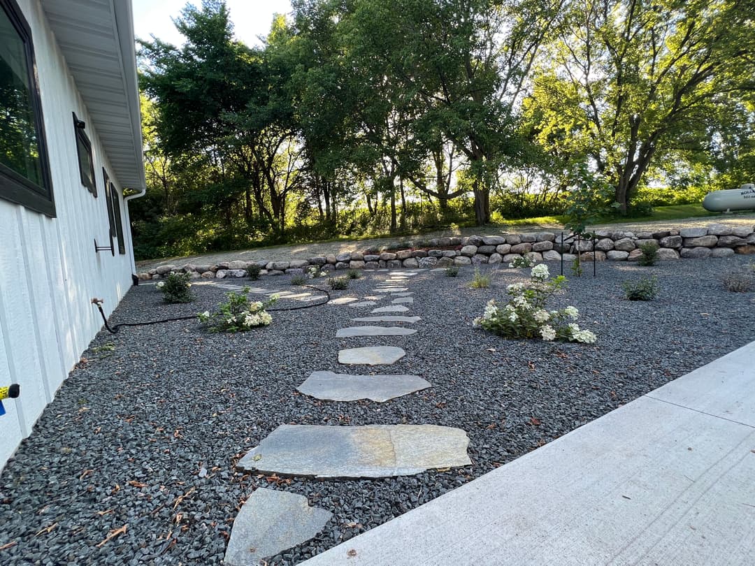 Stone pathway through a landscaped gravel garden with flowers and trees in the background.