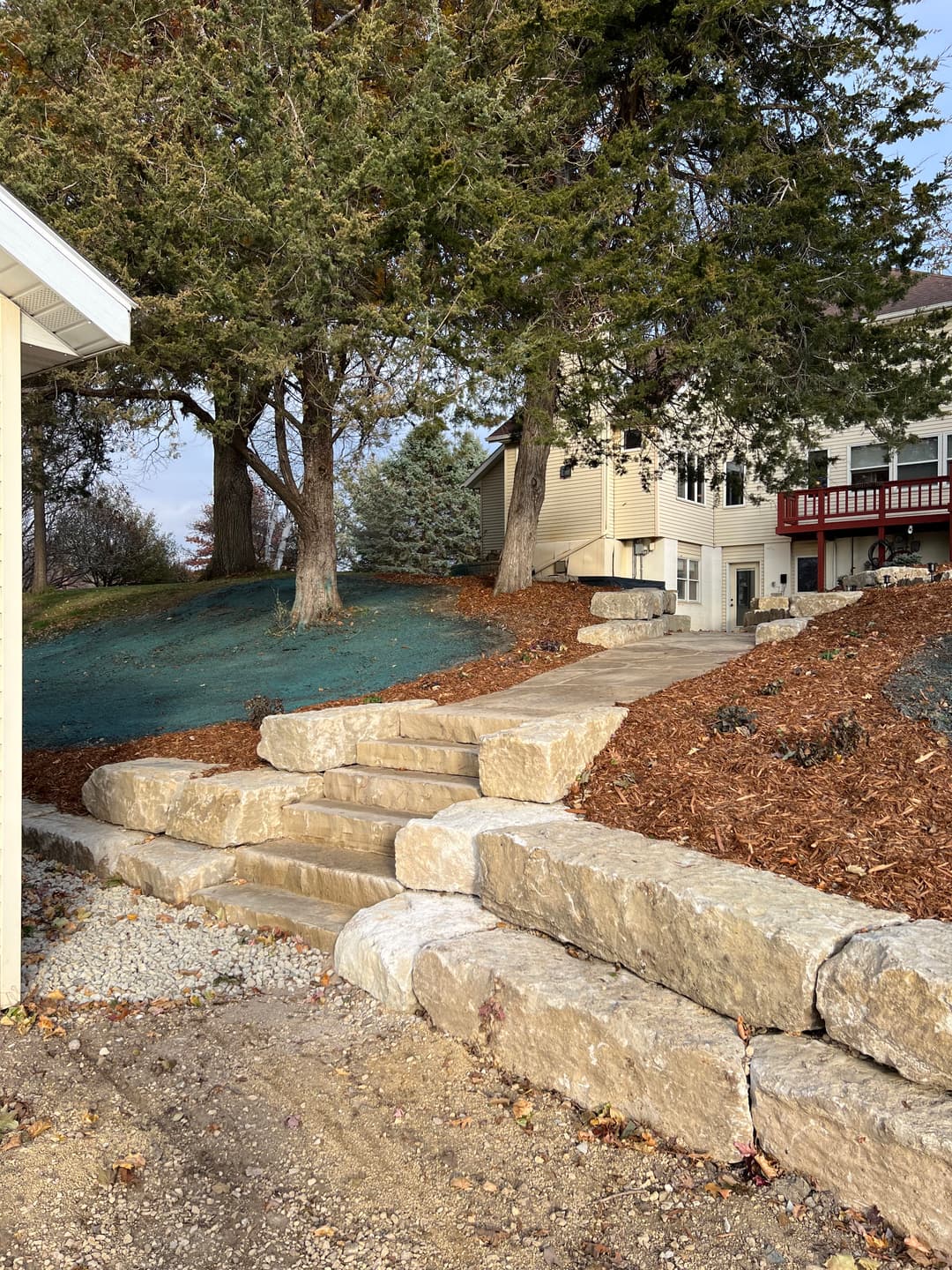 Stone steps leading up to a house with landscaped trees and mulch in the yard.