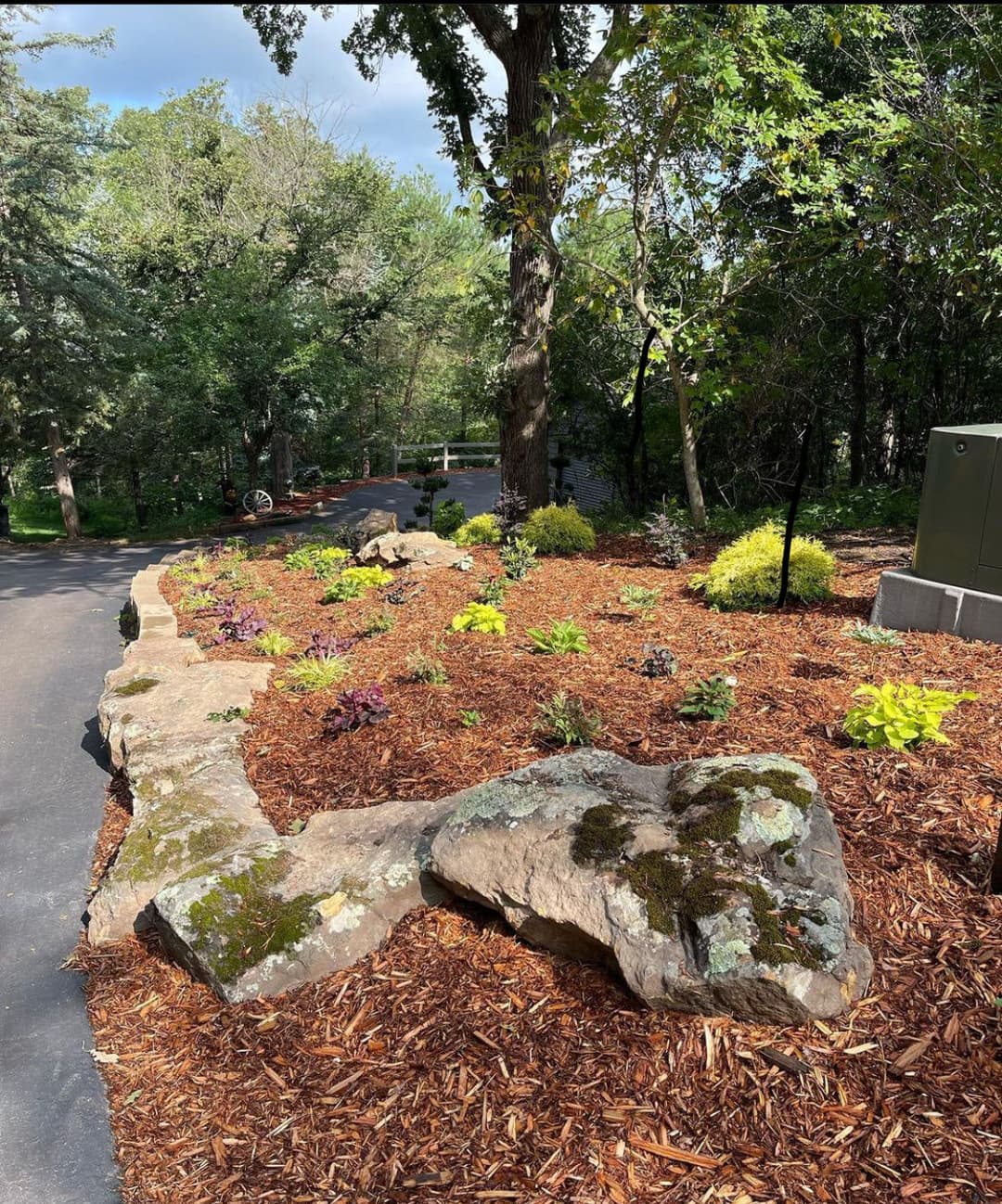 Lush garden landscape with rocks, mulch, and diverse plants along a scenic pathway.