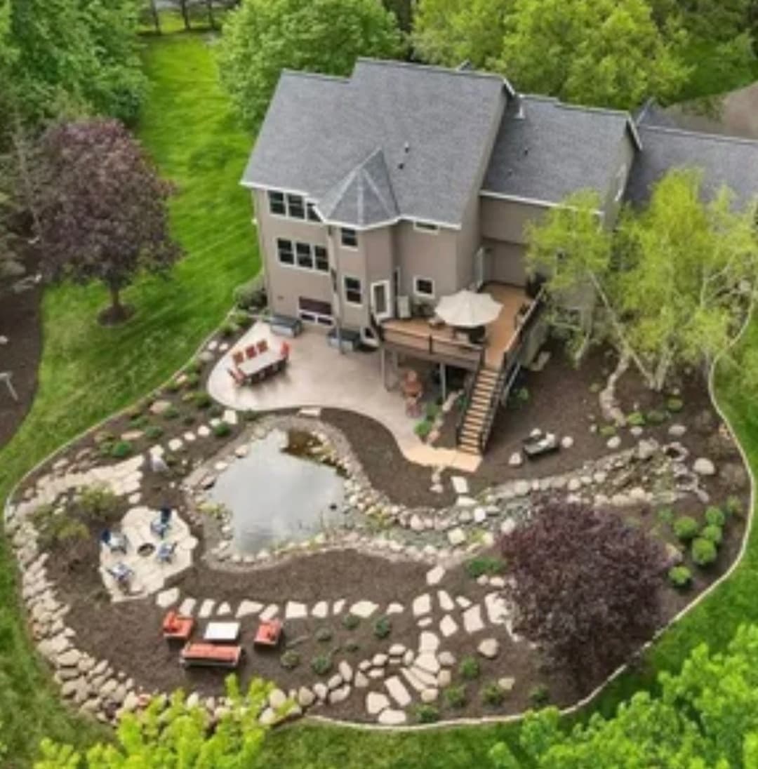 Aerial view of a modern house with landscaped yard, pond, and seating area.