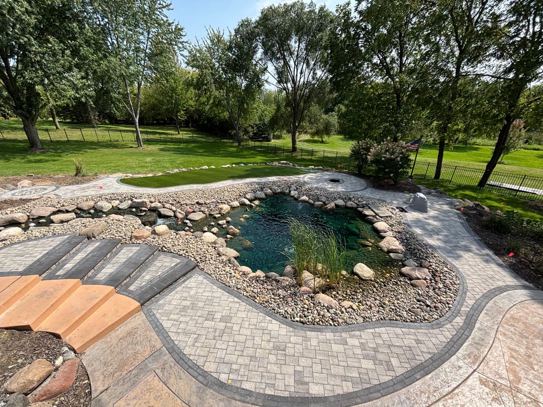 Lush backyard with a pond, stone pathways, and landscaped gardens under a clear blue sky.
