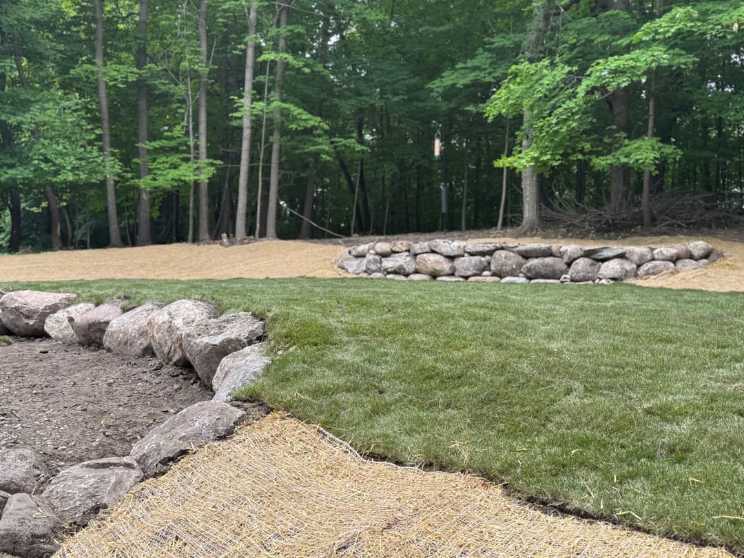 Landscaped area with freshly laid sod, stone border, and tree line in the background.
