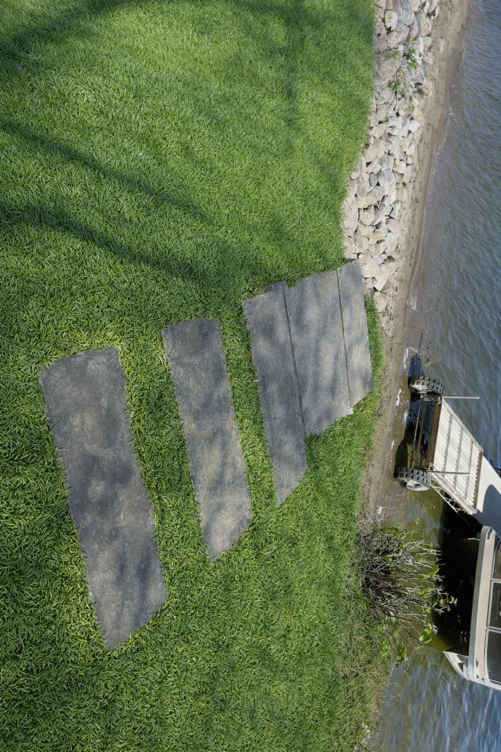 Stone pathway leading to water's edge, surrounded by lush green grass and rocks.