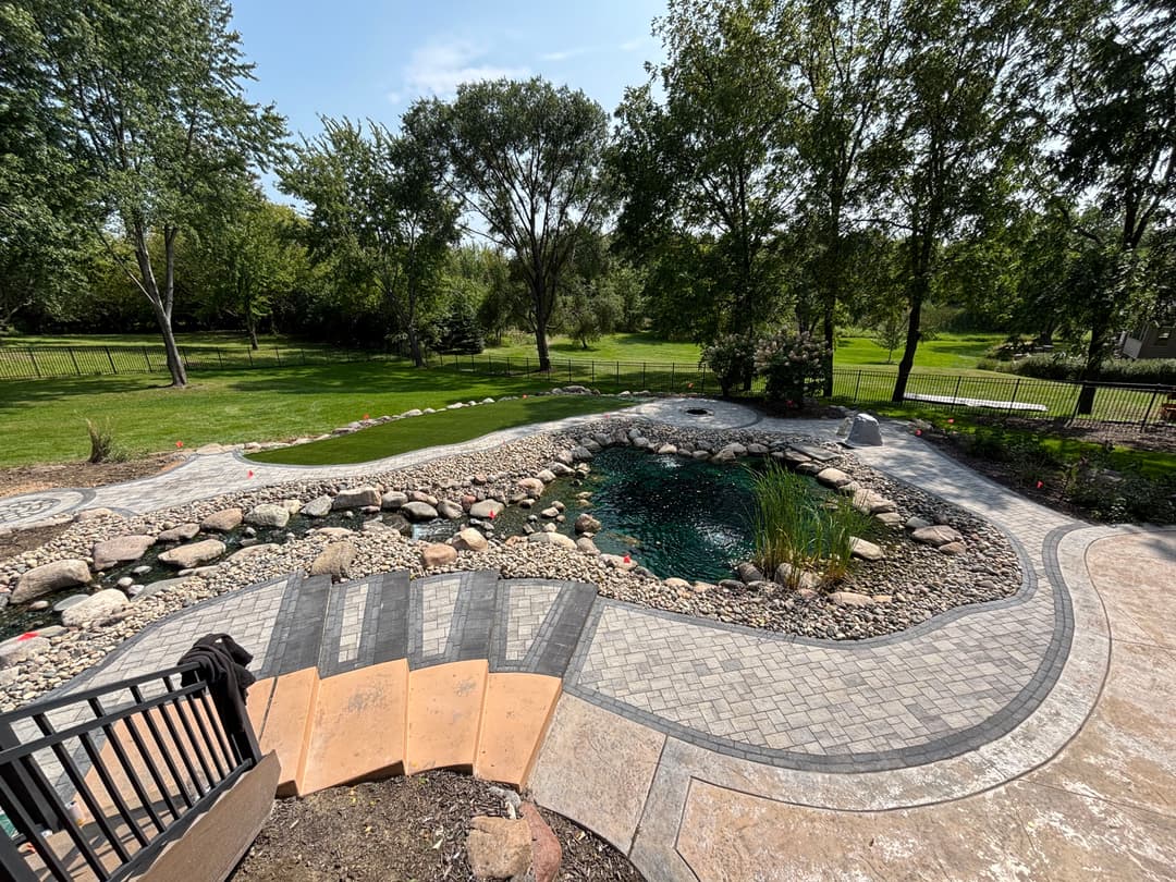 Scenic backyard pond with natural stone landscaping and lush green surroundings.