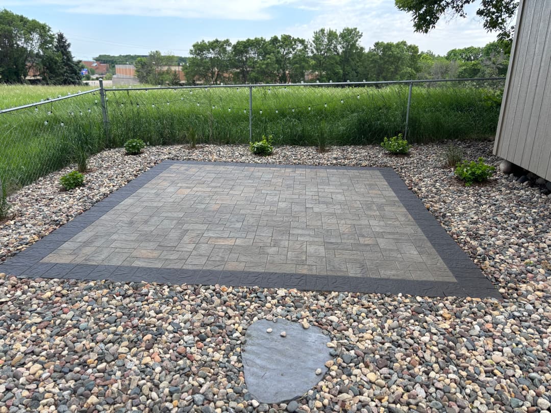 Paved outdoor patio surrounded by decorative rocks and landscaped grass area.