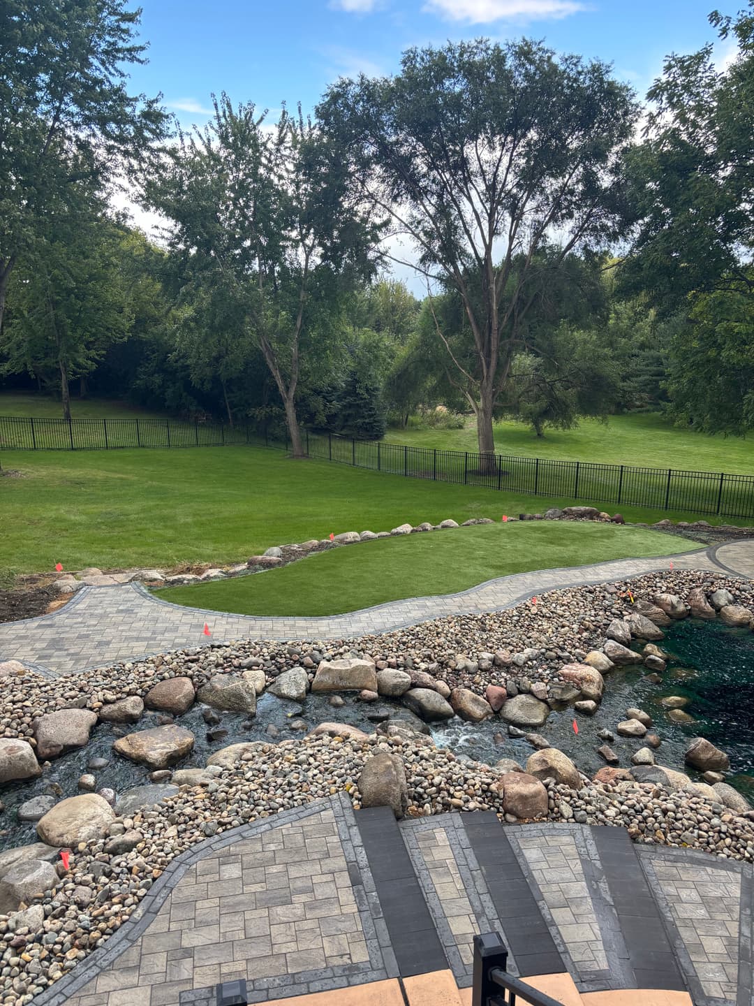 Beautiful landscaped yard with stone pathway, water feature, and vibrant green grass.