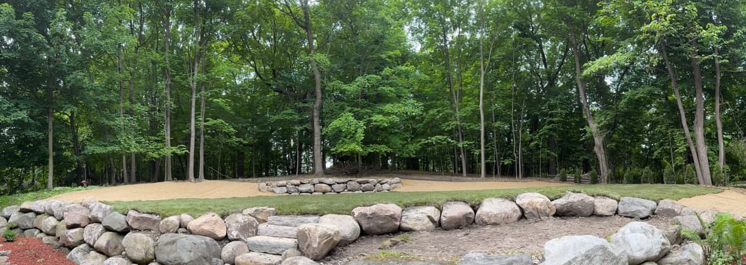 Panoramic view of landscaped garden with stone walls and lush green trees in the background.