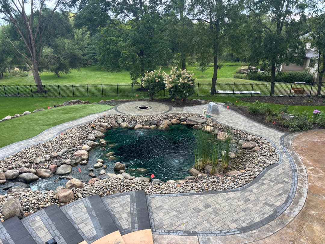 Backyard pond with landscaping, stone border, and lush greenery in a serene setting.