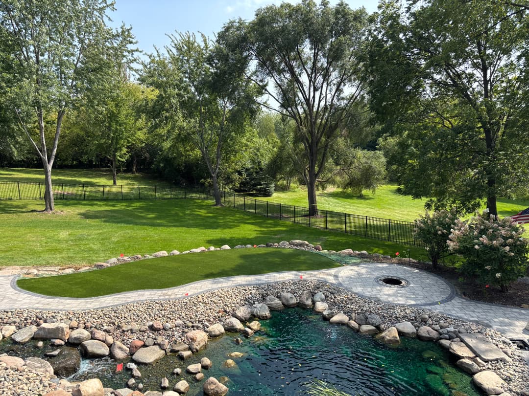 Lush green backyard with a stone path and decorative pond surrounded by trees.