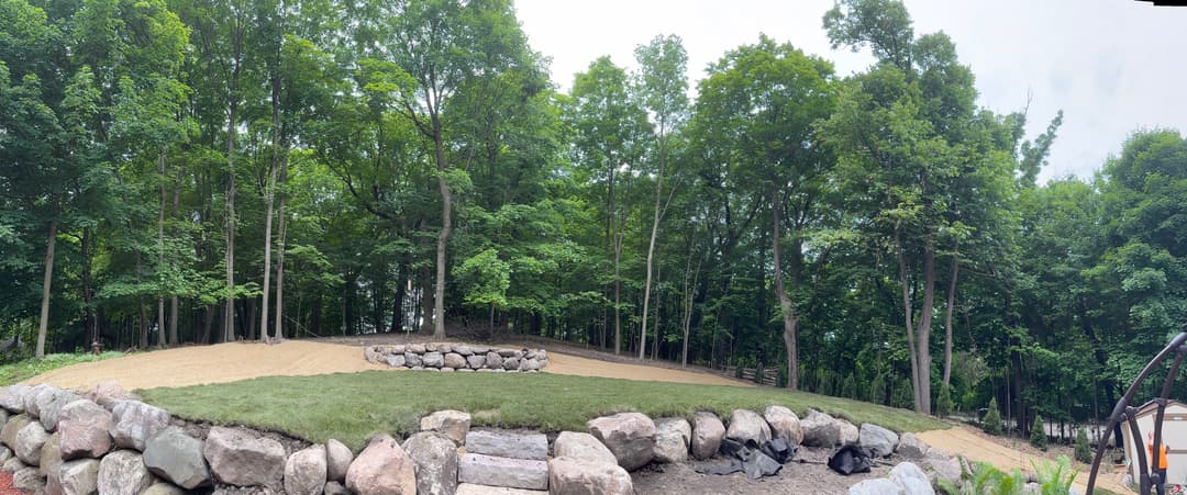 Panoramic view of a landscaped yard featuring a stone fire pit and lush green trees.